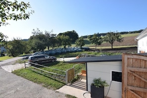 A rural property with a paved driveway, a fenced area with parked cars, and a small building with a wooden door.