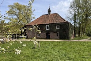Ein Backsteinhaus mit Ziegeldach, einem kleinen Anbau und einer Rasenfläche davor.