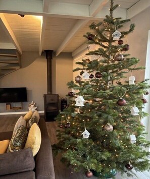 Ein Wohnzimmer mit Weihnachtsbaum, Kamin und einer Couch mit Kissen.
