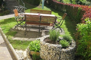 A garden patio with a wooden table and chairs, surrounded by a stone planter and various plants. - Holiday apartment with 1 bedroom (Schönberg)