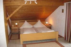 A wooden-framed room with a bed, two bedside tables, and a ceiling light fixture. - Holiday apartment with 1 bedroom (Schönberg)