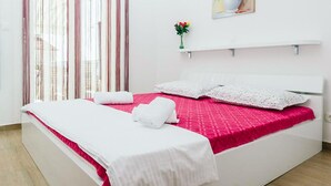 Een hotelkamer met een bed, witte gordijnen, een vaas met bloemen en een schilderij aan de muur.