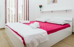 Ein Hotelzimmer mit Bett, weißen Vorhängen, einer Blumenvase und einem Bild an der Wand.