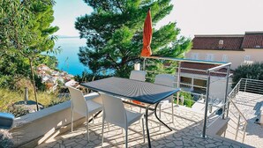 Een terras buiten met een tafel en stoelen, met uitzicht op een kustplaatsje en de zee.