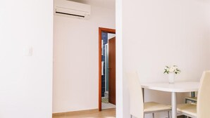 Een kamer met een witte airconditioning, een houten deur naar een badkamer en een kleine ronde tafel met stoelen.