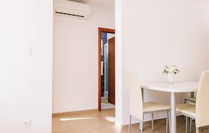 Ein Zimmer mit einer weißen Klimaanlage, einer Holztür zu einem Badezimmer und einem kleinen, runden Tisch mit Stühlen.