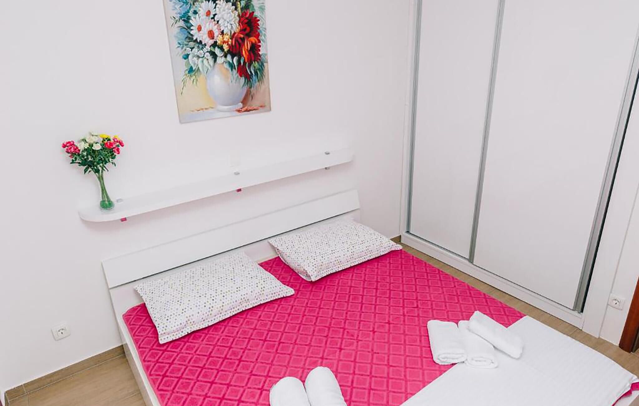 Una habitació d'hotel amb un llit, almoines, una petita estant amb un ram de flors i un quadre a la paret.