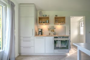 A compact kitchen with white cabinetry, a built-in oven, and a coffee maker. - Holiday apartment "Karla" (Ahrenviölfeld, Deutschland)