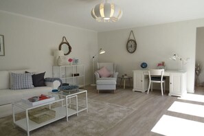 Ein Wohnzimmer mit weißem Sofa, Couchtisch, Schreibtisch, Stuhl und Lampe.