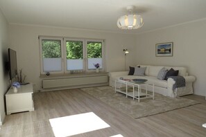 Ein Wohnzimmer mit einem weißen Sofa, einem Couchtisch, einem Fernseher und einer Heizung.