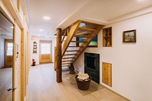 Eine Holztreppe in einer Diele mit Kamin, Holzregalen und einer Tür zu einem weiteren Raum.