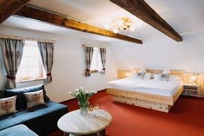 Ein gemütliches Zimmer mit einem Bett, einem Sofa, einem kleinen Tisch mit einer Vase und Gläsern sowie Holzbalken an der Decke.