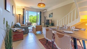 Una sala de estar moderna con un sofá, una mesa de comedor preparada para dos personas, una escalera y vistas a zonas verdes.