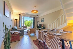 Ein modernes Wohnzimmer mit einer Couch, einem Esstisch für zwei Personen, einer Treppe und Blick ins Grüne.
