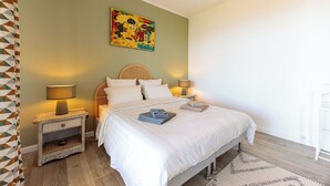 Un dormitorio con una cama, dos mesitas de noche con lámparas, un cuadro en la pared y una alfombra estampada.