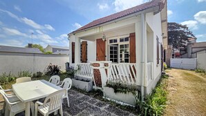 Une petite maison avec une véranda, une table entourée de chaises et un jardin.