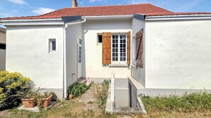 Un bâtiment blanc avec un toit recouvert de tuiles rouges, une petite fenêtre et des volets en bois.