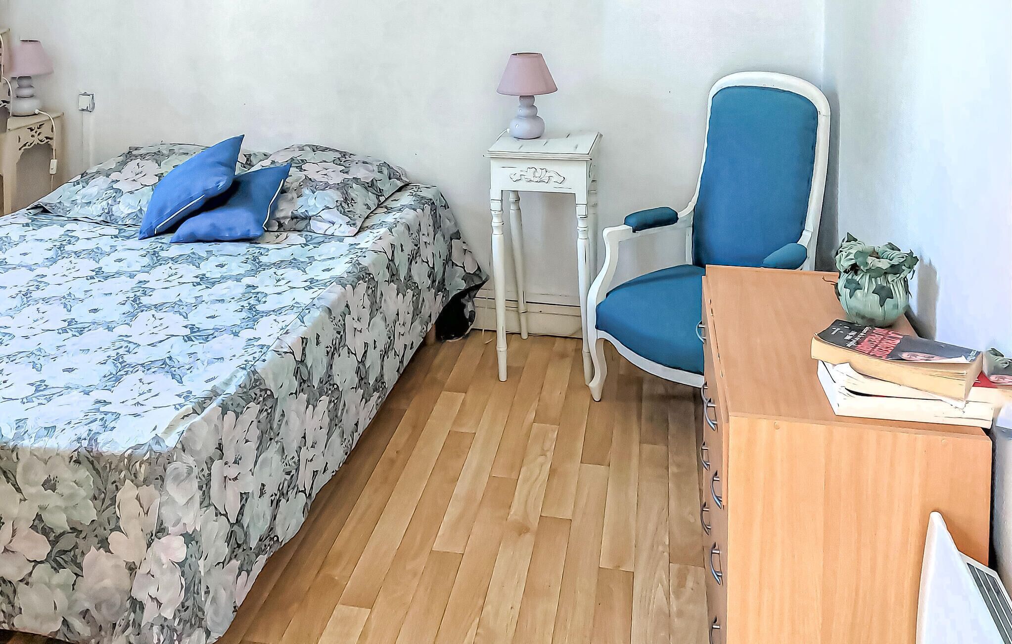 Un dormitorio con cama, una silla, una mesita y un escritorio con libros.