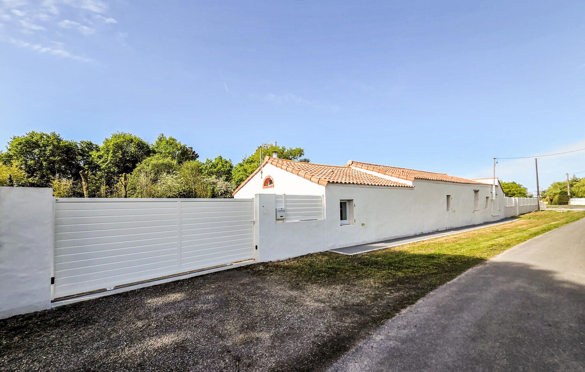A long, white building with a tiled roof, a gated entrance, and a paved driveway.