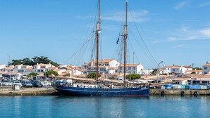 Ein Hafen mit einem großen Segelschiff an einem Anlegesteg, umgeben von Wohnhäusern mit roten Ziegeldächern.