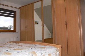 A bedroom with a bed, wooden wardrobe, and a window. - Holiday apartment with 1 bedroom (Hilmersdorf)