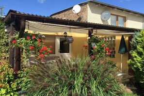 Ein Haus mit überdachter Veranda, Satellitenschüsseln und einem Garten mit roten Blumen.