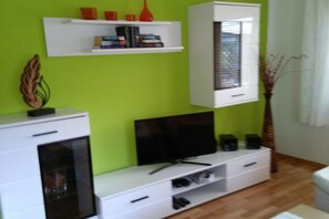 Ein Wohnzimmer mit Fernseher, weißem Unterhaltungsschrank und einem Regal mit Büchern und Dekoration.
