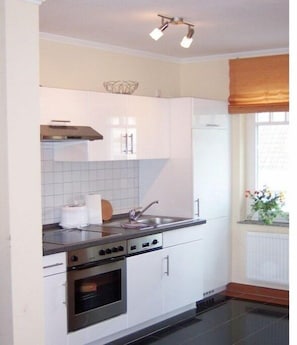 A kitchen with white cabinets, a stainless steel oven, a sink, and a window with a view. - No. 08 "Villa Laetitia" in Binz (Ostseebad Binz)