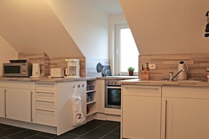 Una cocina moderna con armarios blancos, un microondas, una cafetera, un hervidor, un tostador y un horno pequeño.