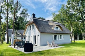 A white house with a grey roof, a chimney, and a patio with chairs and a grill. - Holiday home Lake & Countryside (Zirchow)