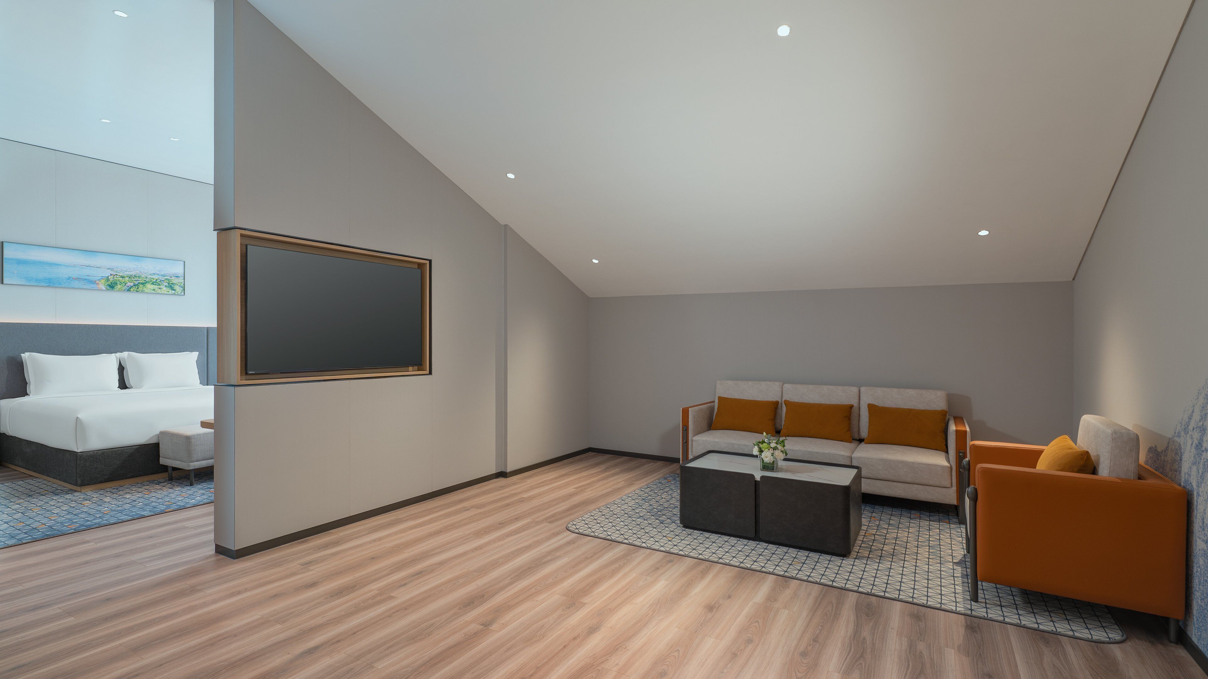 A modern hotel room with a bed, a sofa, a coffee table, and a TV mounted on the wall.