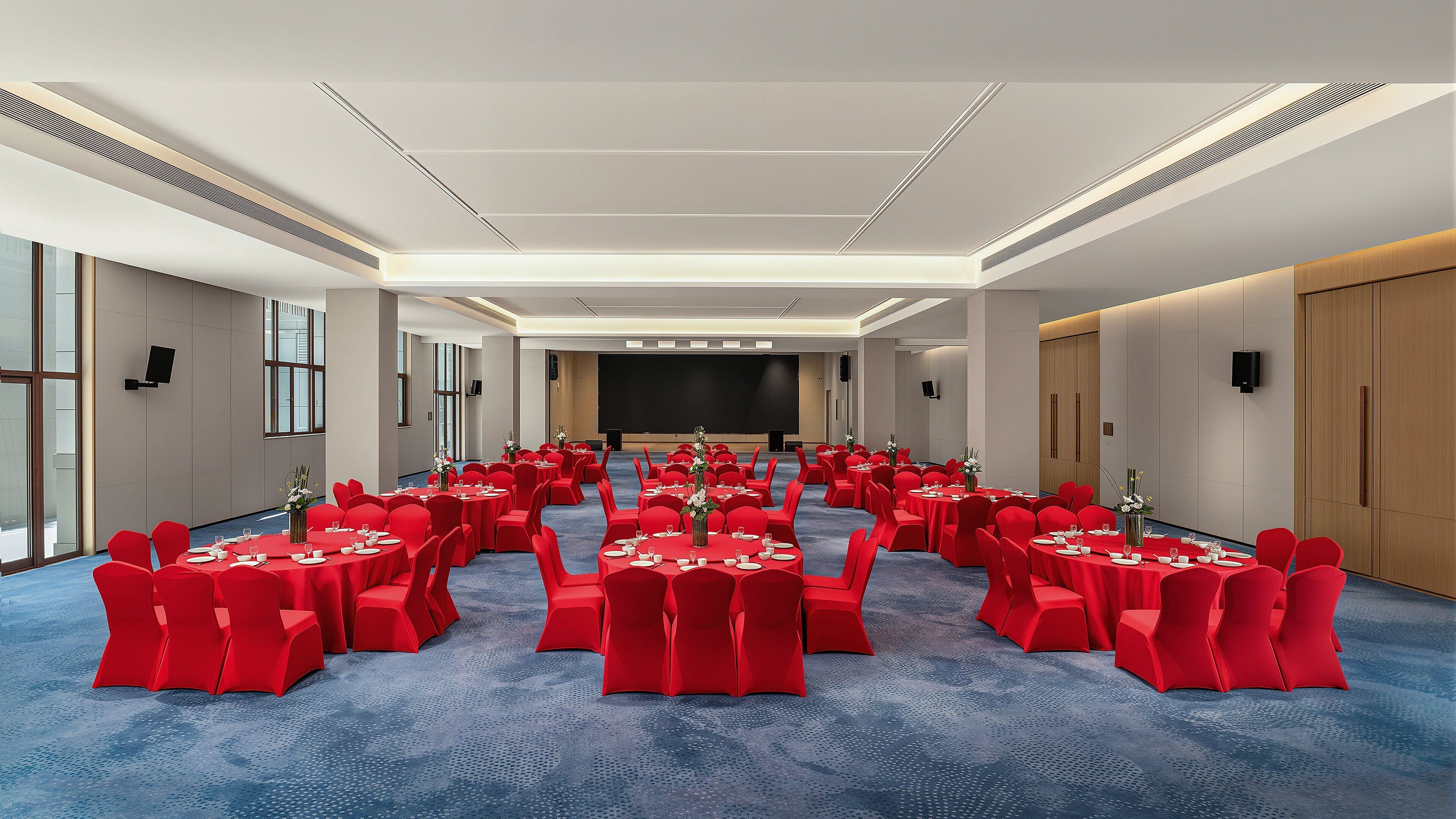 A conference room with round tables, red chairs, and a large screen at the front.