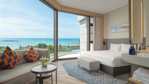 A hotel room with a bed, a sofa, a small table, and a view of the ocean.