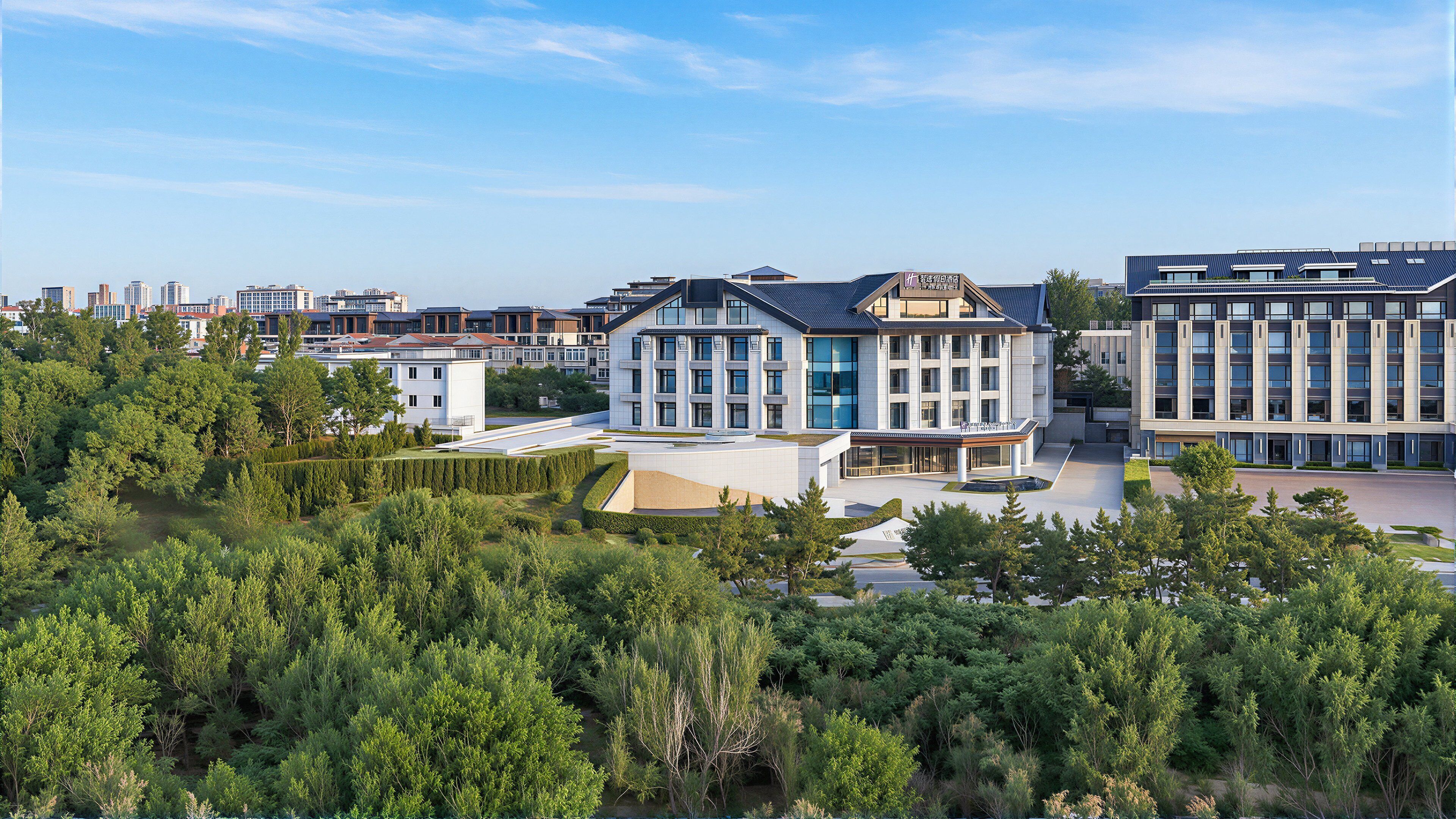 A modern building complex with multiple structures, surrounded by dense greenery.