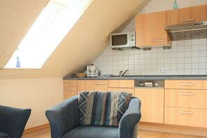 Eine Küche mit Mikrowelle, Kaffeemaschine und Geschirrspüler. Über der Spüle befindet sich ein Fenster, und ein Stuhl mit einem gemusterten Sitzkissen.