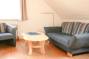 Ein gemütliches Schlafzimmer im Loft-Stil mit schräg versiegelter Decke, zwei grauen Sofas, einem Holztisch und einer Heizung.