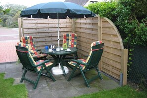 Eine Terrasse mit einem runden Tisch, vier Stühlen und einem großen Sonnenschirm.