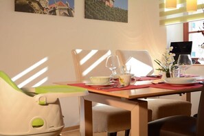 Ein Essbereich mit Tisch für zwei Personen, Stühlen, einem Laptop und einem Fenster mit Tageslicht.