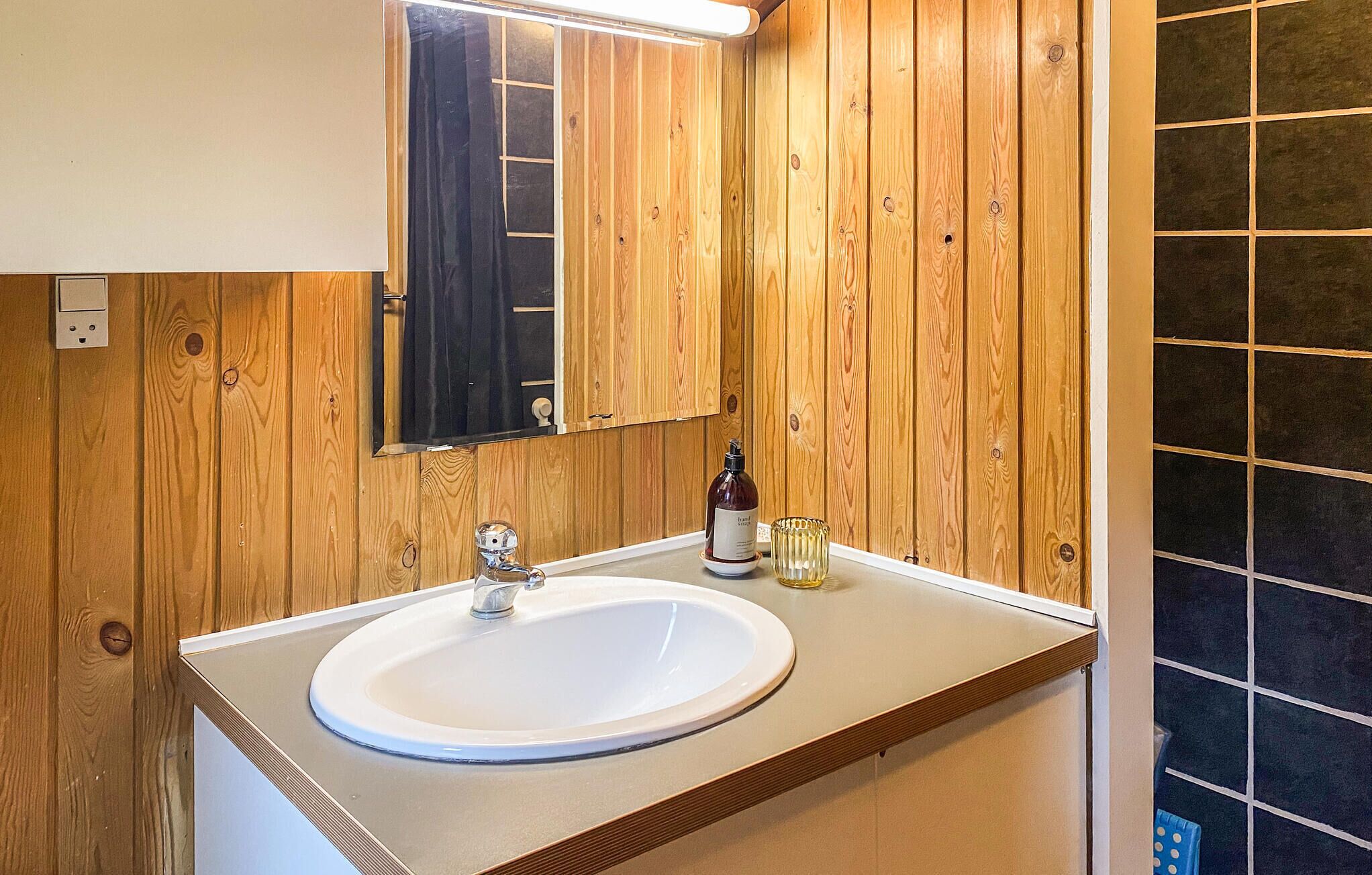 Ein Badezimmer mit einer Holzwand, einem weißen Waschbecken, einem Spiegel und einer Handseifenflasche.
