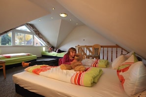 Een studentenkamer met een schuine kap, een raam, een bed met kussens en een stoel.