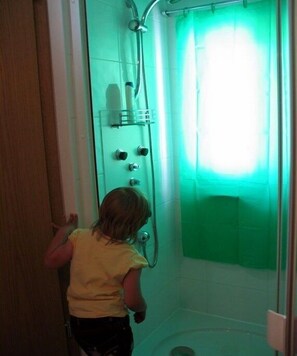 Un bagno con doccia, tenda verde e parete rivestita di piastrelle bianche.
