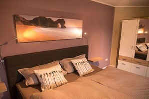 Ein Schlafzimmer mit Bett, Kissen, Nachttisch, Kleiderschrank und einem Bild an der Wand.