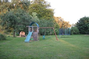 Ein Spielplatz mit Rutsche, Schaukeln und Klettergerüst in einer grünen Parkanlage mit Bäumen.