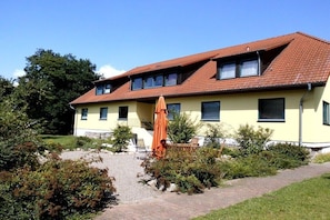 Ein zweistöckiges Haus mit rotem Ziegeldach, einer gelben Fassade und einer Einfahrt mit Kies.