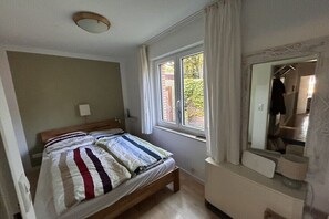 Ein Schlafzimmer mit Bett, Fenster, Spiegel und Kommode.