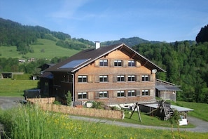Ein mehrstöckiges Gebäude mit Satteldach, Solaranlage und Holzzaun in ländlicher Umgebung.