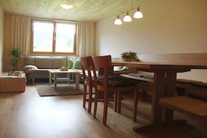 Ein gemütliches Wohnzimmer mit einem Holzesstisch, Stühlen, einer Couch und einem Fenster mit Vorhängen.