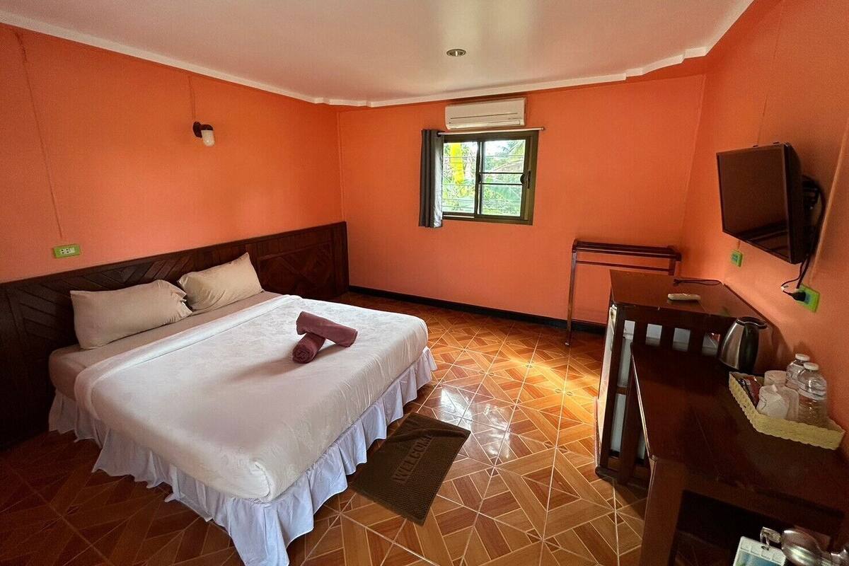 A hotel room with a bed, a desk, a chair, an air conditioning unit, and a television.