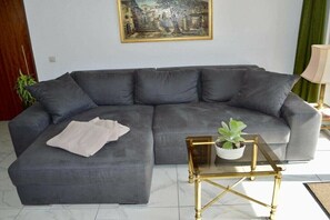 A grey sofa with a white throw blanket, a glass coffee table with a plant, and a painting on the wall. - Holiday apartment with 3 bedrooms (Herrischried)