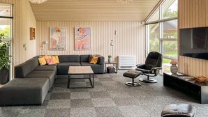 Una sala de estar moderna con un sofá modular, una mesa de centro, un sillón de cuero negro y un televisor en la pared.